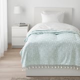 Jeté GOKVÄLLÅ bleu avec motifs géométriques blancs sur le lit.