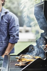 Homme grillant du maïs sur un barbecue GRILLSKÄR, chemise bleue.
