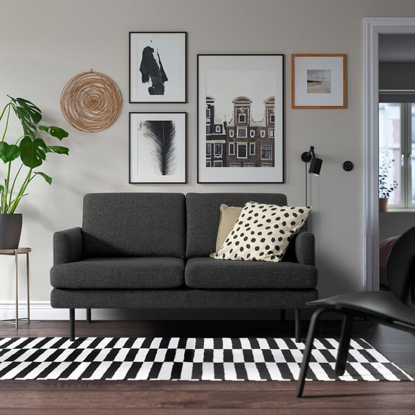 Salon moderne : canapé GRILLSTORP gris avec coussins, tapis noir et blanc, plante, art mural. Confortable et élégant.