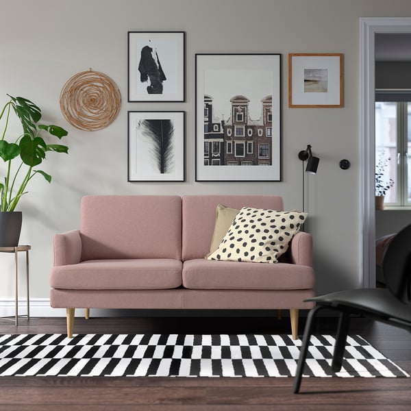 Canapé GRILLSTORP rose avec pieds en bois, mur d’art, coussins, oreiller à pois et tapis noir et blanc dans un salon confortable.