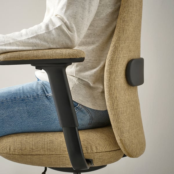 Une personne assise sur une chaise de bureau réglable, accoudoirs visibles, vêtue d’un jean et d’un pull de couleur claire.