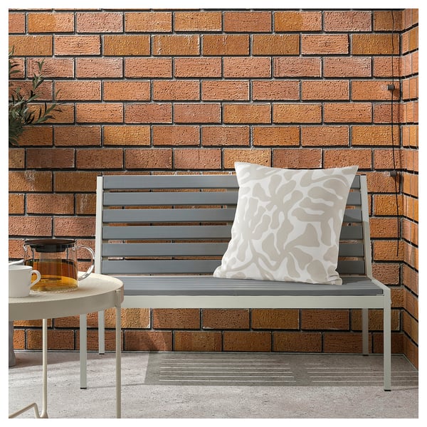 Banc d’extérieur moderne avec coussin gris et oreiller à motifs contre mur de briques.
