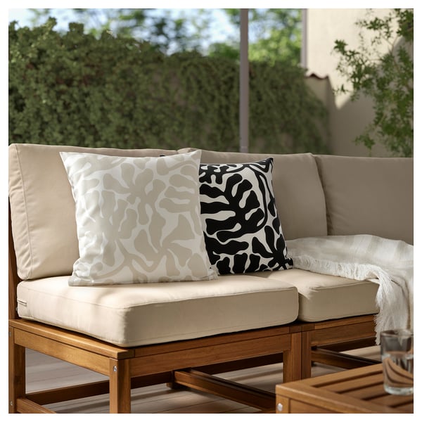 Canapé de patio avec deux coussins à motifs. Beige avec des tourbillons noir/blanc. Cadre extérieur avec verdure.
