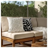Canapé de patio avec deux coussins à motifs. Beige avec des tourbillons noir/blanc. Cadre extérieur avec verdure.
