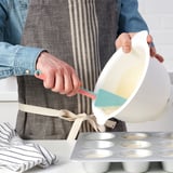 Une personne verse la pâte d’un bol dans des moules à muffins à l’aide d’une spatule en silicone flexible, en veillant à ce qu’il n’y ait pas de gaspillage.