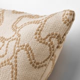 Gros plan d’un coussin blanc cassé avec un motif tissé beige complexe, mettant en valeur un design jacquard de haute qualité.