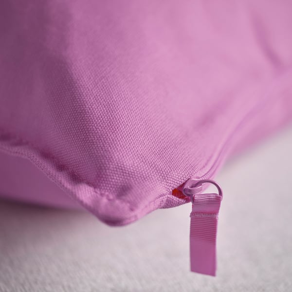 Gros plan d’une housse de coussin rose douce et unie avec fermeture éclair, montrant la texture et la qualité.