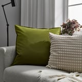 Oreiller GURLI vert vif, oreiller blanc texturé, couverture douillette sur canapé gris, près de grande fenêtre, lampes modernes.