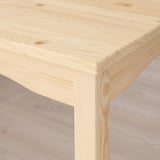 Gros plan d’un coin de table en bois clair et robuste, mettant en valeur le grain et la finition lisses et naturels du pin.