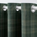 Des rideaux en tartan vert foncé avec œillets pendent soigneusement, offrant un assombrissement et une intimité.