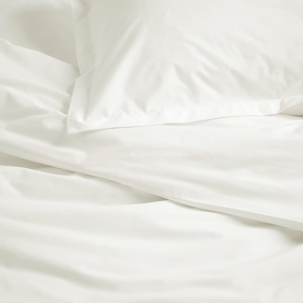 Parure de lit d’un blanc éclatant avec percale de coton lisse, mettant en valeur des coutures soignées et un savoir-faire de qualité.