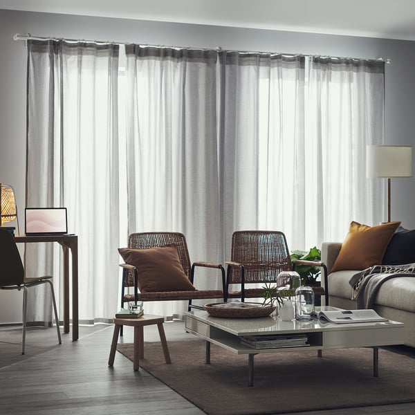 Chaises en osier, canapé, table basse, bureau avec ordinateur portable, lampadaire, rideaux transparents.
