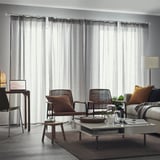 Chaises en osier, canapé, table basse, bureau avec ordinateur portable, lampadaire, rideaux transparents.