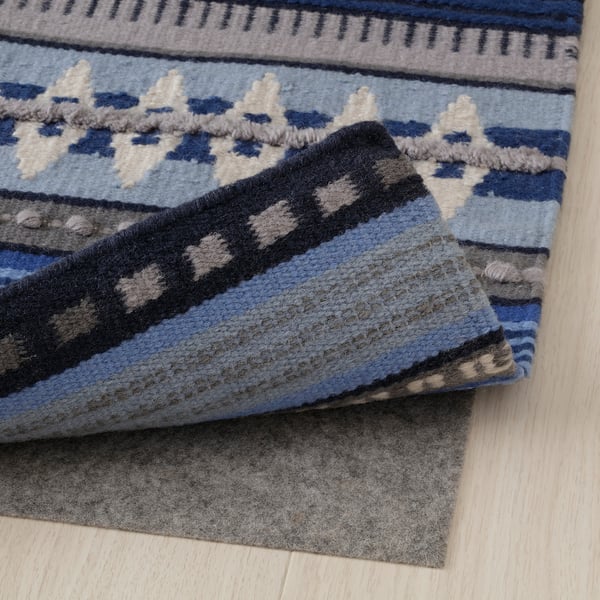 Coin de tapis tissé à la main bleu, gris et noir avec sous-couche antidérapante sur plancher en bois.