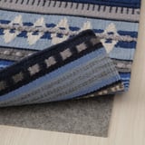 Coin de tapis tissé à la main bleu, gris et noir avec sous-couche antidérapante sur plancher en bois.