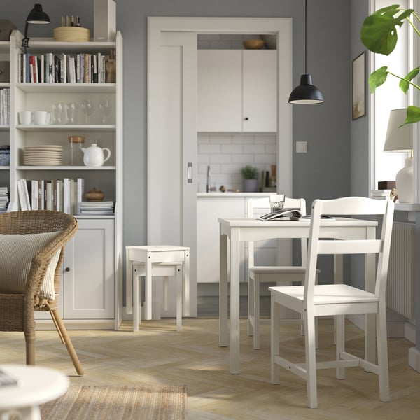 Petite table à manger et chaises en bois blanc. Design épuré et moderne. Fait partie de la série HAUGA. Murs gris clair et parquet en bois naturel.