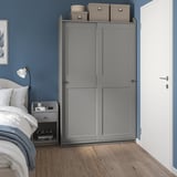 Chambre bleue minimaliste avec armoire HAUGA grise, parquet, lit blanc et table de chevet avec lampe.