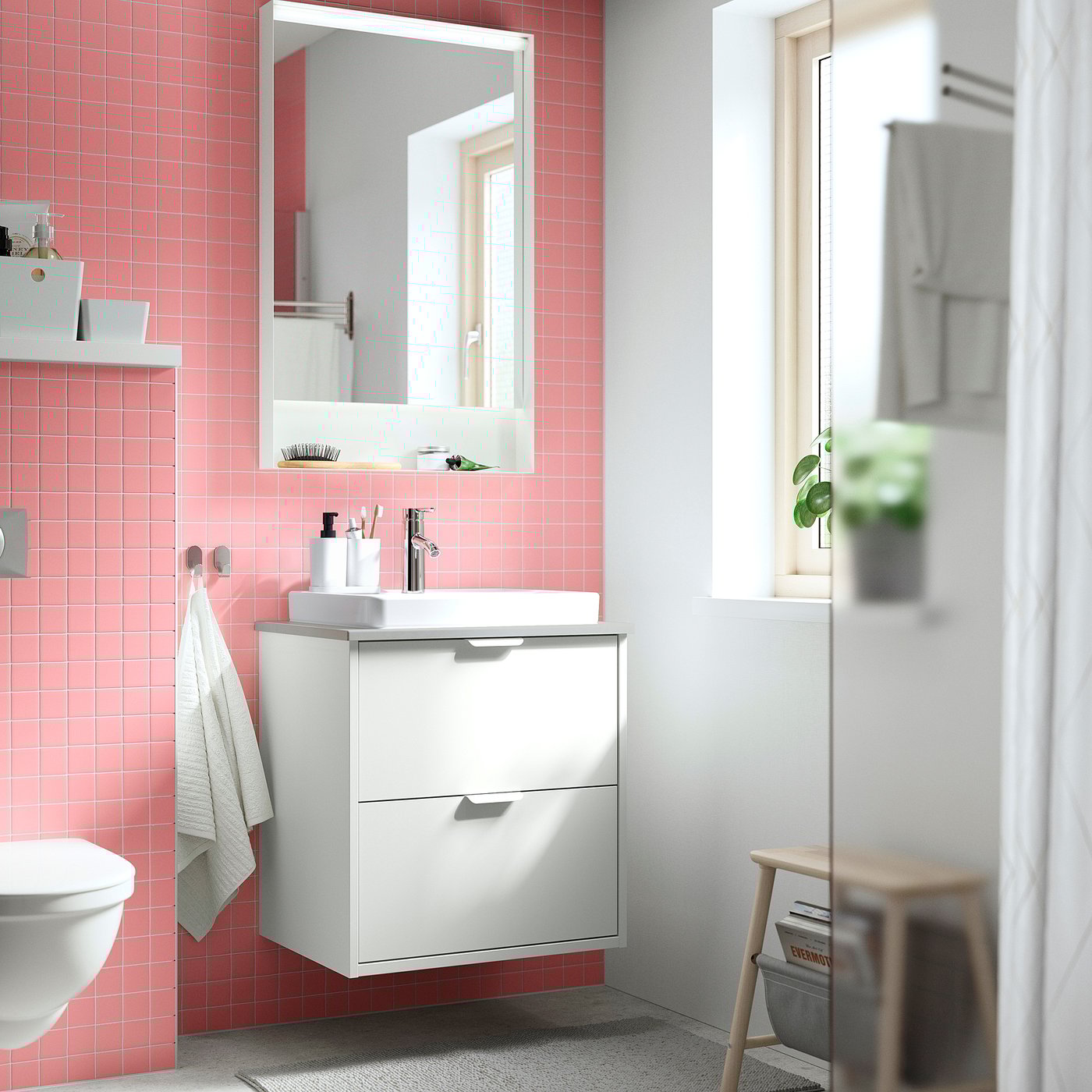 Salle de bain moderne avec meuble-lavabo mural HAVBÄCK, deux tiroirs, carrelage rose, miroir et tabouret près de la douche.