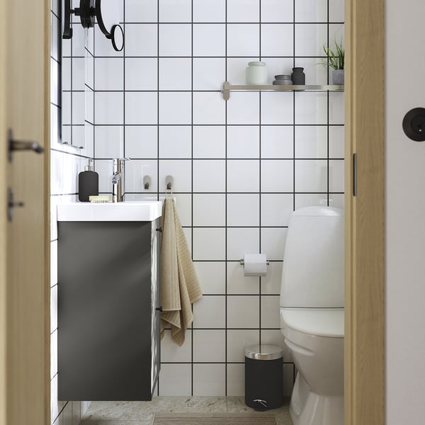 Salle de bain moderne avec vanité noire, toilettes blanches et murs carrelés. Vanité murale avec deux tiroirs, serviette à proximité.