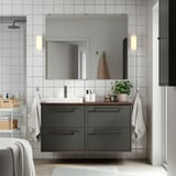 Salle de bain moderne avec meuble-lavabo HAVBÄCK gris foncé, plusieurs tiroirs, lavabo blanc, grand miroir et serviettes murales.