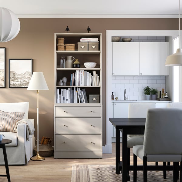 Salon moderne avec unité de rangement HAVSTA contenant des livres, un canapé, une petite table à manger et une lampe, un éclairage chaleureux.