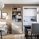 Salon moderne avec unité de rangement HAVSTA contenant des livres, un canapé, une petite table à manger et une lampe, un éclairage chaleureux.