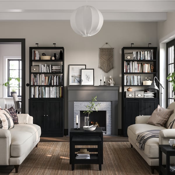 Salon moderne avec étagère noire HAVSTA, canapés crème, tapis gris, cheminée.