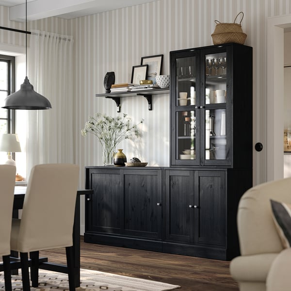 Salle à manger moderne avec armoire HAVSTA, verrerie, décorée de cadres, de vases et d’un panier. Rangement en pin, chaises beiges et lampe.