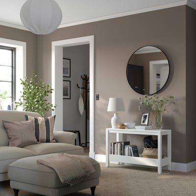 Salon confortable avec console en pin, canapé beige, coussins rayés, miroir, lampe, livres, couvertures, fleurs, plante.