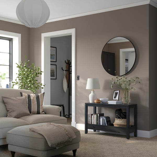 Salon moderne avec console HAVSTA, miroir rond, plantes, lampe et canapé gris avec oreillers rayés et plaid beige.