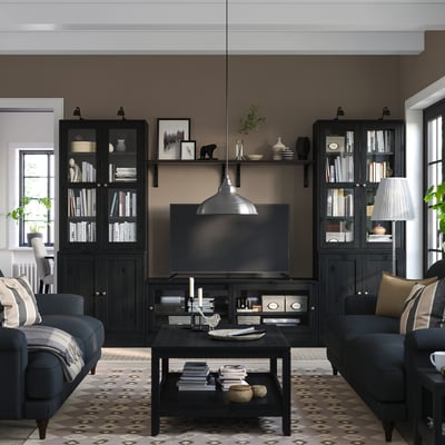 Salon moderne avec des meubles en bois sombre, une télévision à écran plat, des étagères et des sièges confortables. Stylisé avec une lampe et un décor.