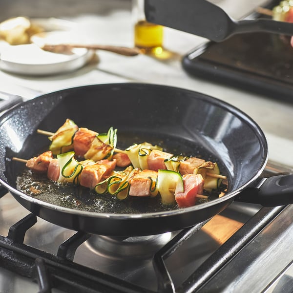 Poêle à frire noire HEMLAGAD cuisson des brochettes sur la cuisinière avec revêtement antiadhésif.