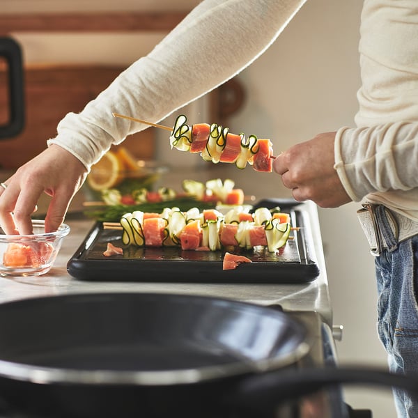La personne assemble des brochettes avec du saumon et des légumes à l’aide d’une poêle à frire antiadhésive sur une cuisinière.