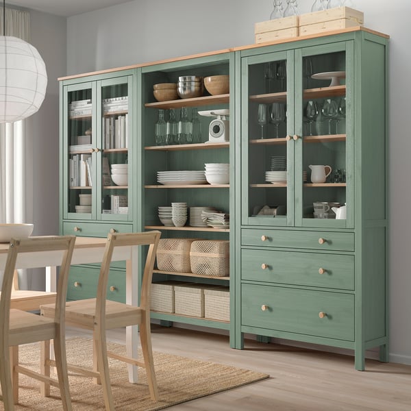 Unité de rangement HEMNES verte, portes vitrées, étagères en bois, bols, vaisselle, verres à vin, livres, chaises.