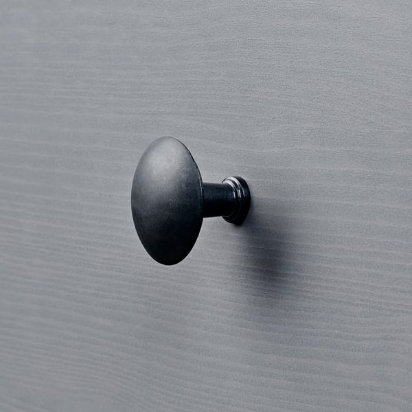 Petit crochet circulaire noir sur un mur gris texturé.