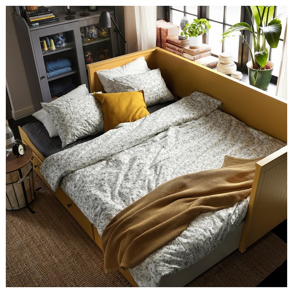 Lit de jour HEMNES jaune vif avec literie florale, deux oreillers et des tiroirs de rangement.