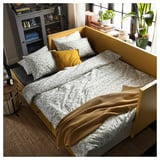 Lit de jour HEMNES jaune vif avec literie florale, deux oreillers et des tiroirs de rangement.