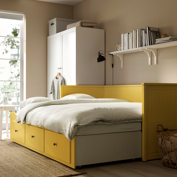 Lit de jour HEMNES jaune vif, soigneusement placé sous les étagères blanches près du mur, à côté d’un grand placard, aménageant les petits espaces avec un lit double coulissant.