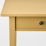 Gros plan d’une table en bois jaune avec une finition lisse et élégante et une poignée de tiroir circulaire.