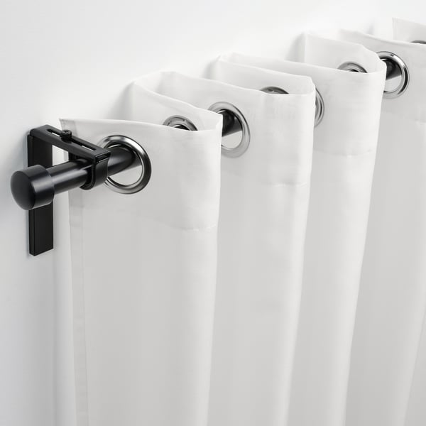 Deux rideaux blancs sont suspendus à des tringles noires avec des œillets circulaires, laissant passer la lumière tout en offrant de l’intimité.
