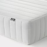 Un coin d’un matelas IKEA blanc et ferme présentant des coutures diagonales et une étiquette noire.