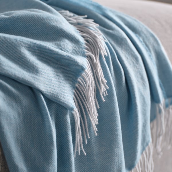 Plaid doux bleu clair avec des bords frangés drapé sur un objet.