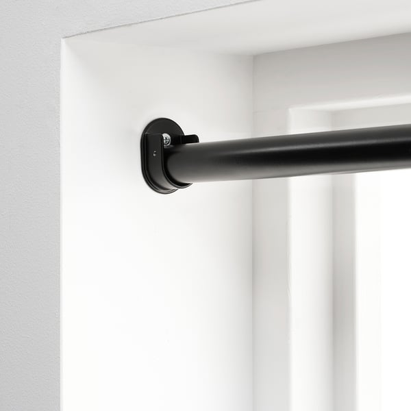 Support de tringle à rideau noir monté sur un mur blanc, faisant partie du système HUGAD pour suspendre des rideaux entre deux murs opposés.