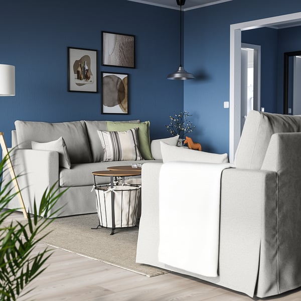 Salon bleu confortable avec canapé gris HYLTARP, table basse blanche, lampe suspendue, art et plante.