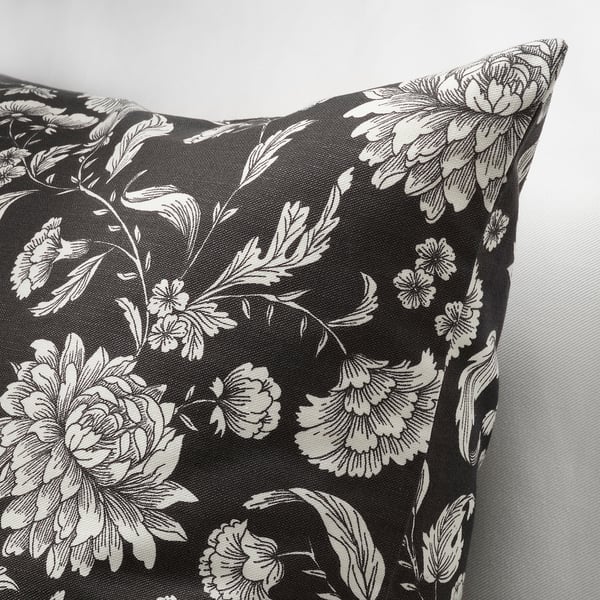 Oreiller noir avec motif floral blanc, détails complexes, tissu lisse, vu de côté.