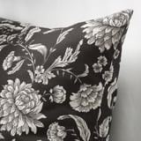 Oreiller noir avec motif floral blanc, détails complexes, tissu lisse, vu de côté.