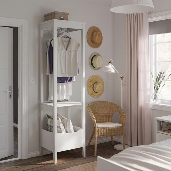 Chambre moderne avec armoire blanche IDANÄS, chaise en osier et chapeaux au mur.