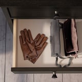 Des gants en cuir marron et un parapluie compact sont suspendus sur une étagère sombre, fond marron et beige.