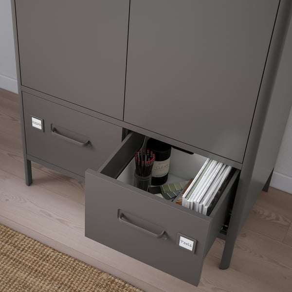 L’armoire de bureau grise ouverte révèle des outils et des dossiers organisés dans le tiroir du bas, étiquetés outils.
