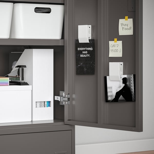 Armoire grise ouverte affichant un rangement organisé : bacs blancs, notes et affiche de motivation.